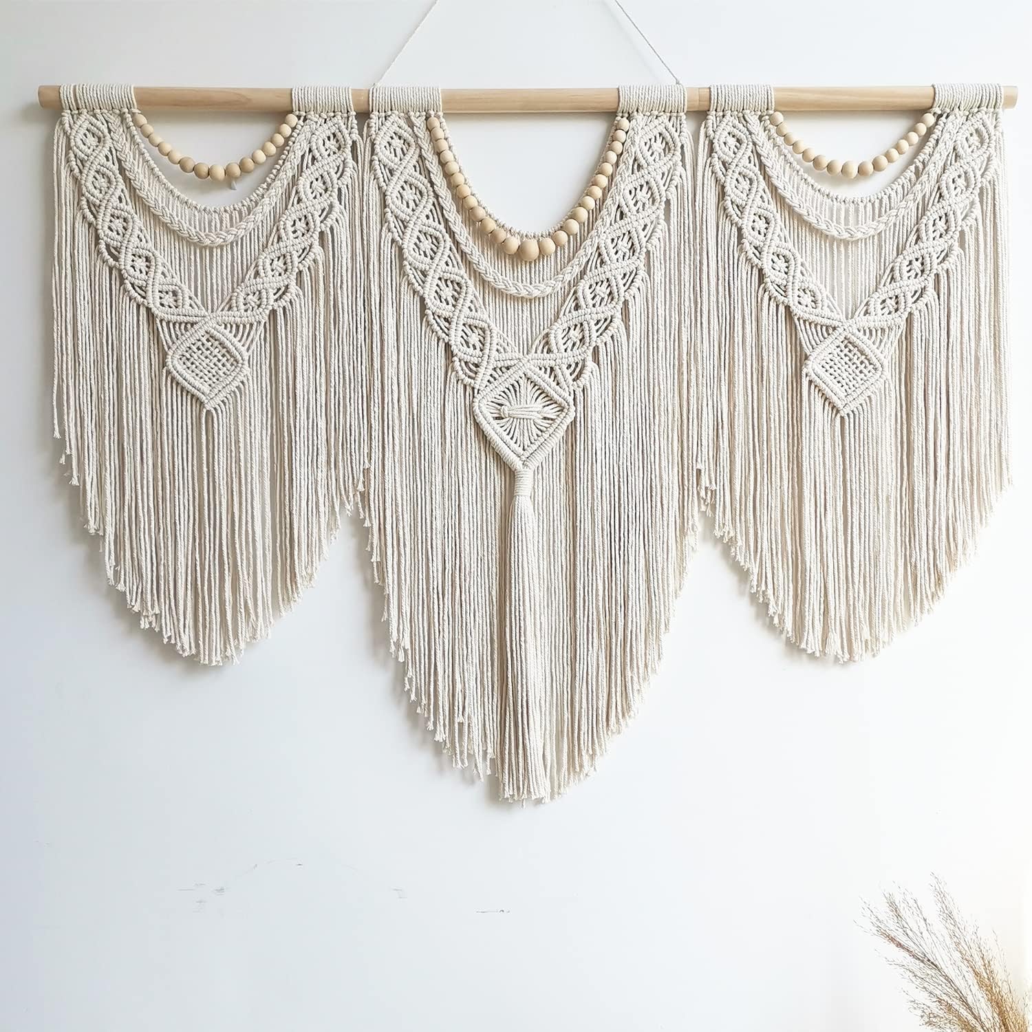 Large boho macrame wall hanging with geometric design and cotton tassels displayed on a living room wall